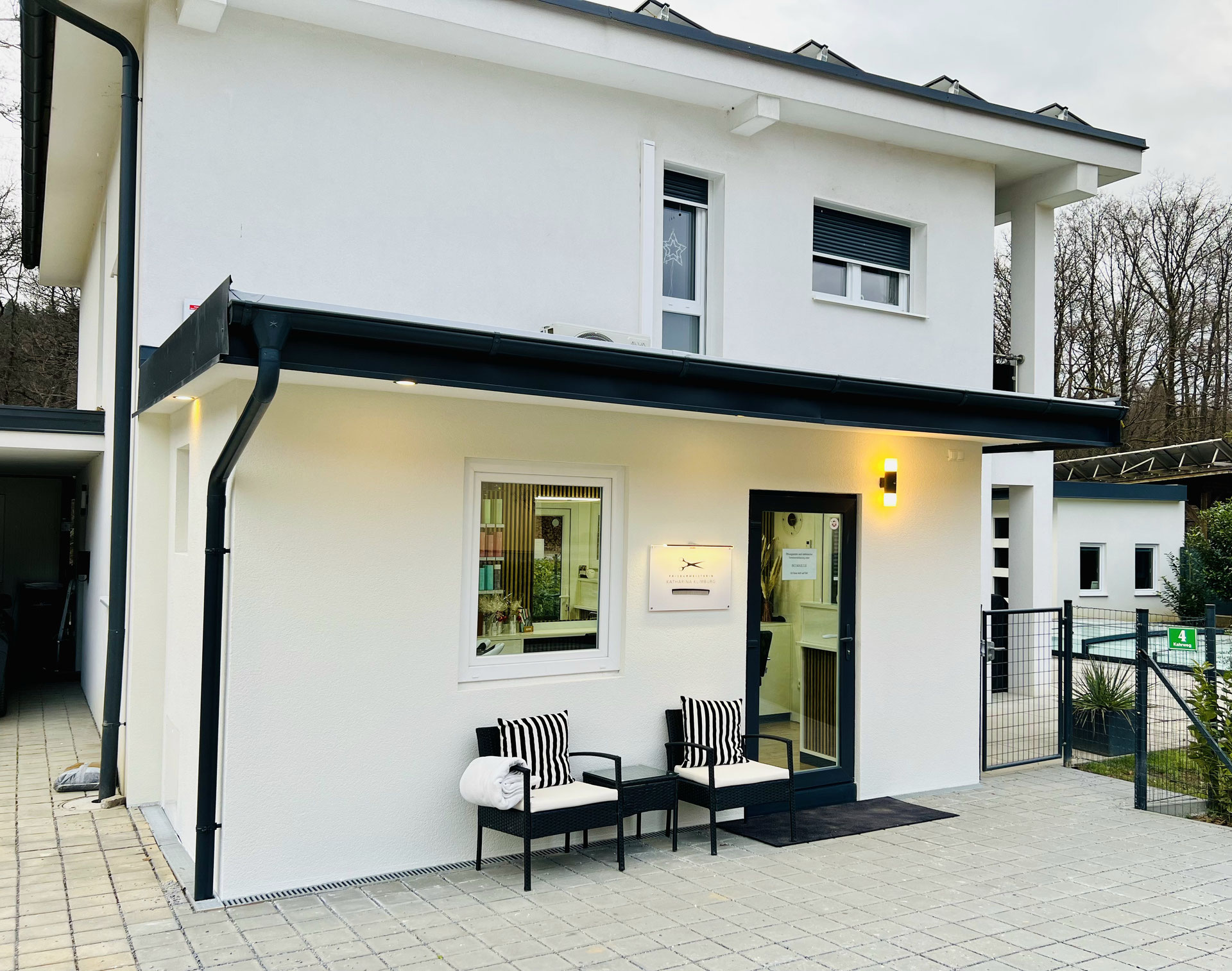 Salon-Außenansicht mit Eingangsbereich, Sitzgelegenheit und Tafel mit Schere-Logo.