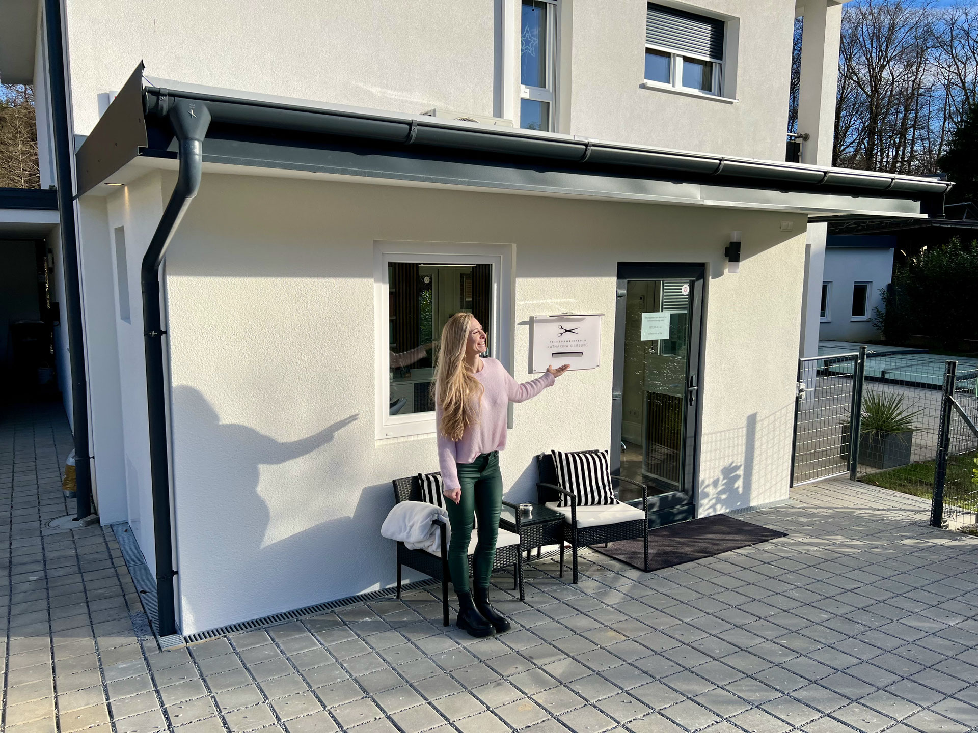 Katharina Klimburg vor dem Salon-Eingang, Schild mit Schere als Logo, sonniger Vormittag.