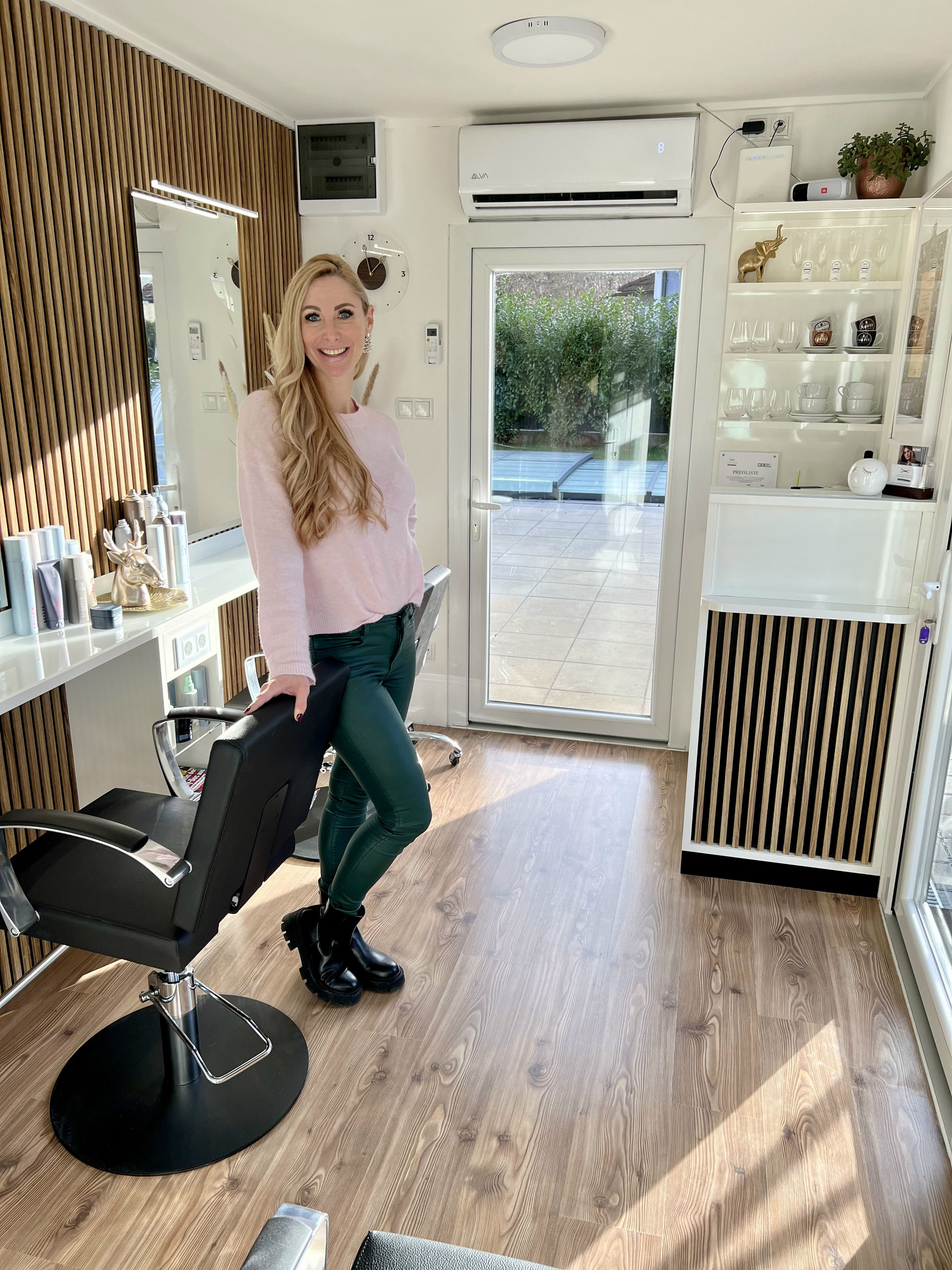 Katharina Klimburg in ihrem Salon in Tobelbad – heller Raum mit Holzpaneelen, weißer Friseurstuhl, Blick auf Garten.